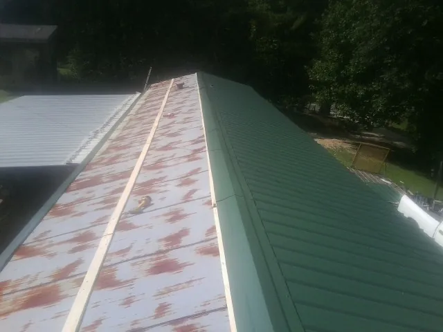 Old rusted panels beside newly installed green metal roofing — Wind Damage Roof Repair by Roofing Brothers in Hanover