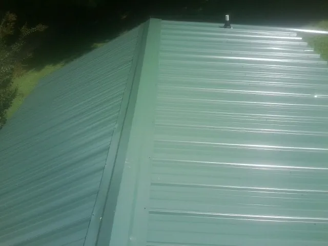 New green metal panels meeting at the ridge of a roof — Flat Roof Repair work by our crew in Hanover